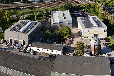 Campus Weigelstraße Drohnenaufnahme vom Campus mit mehrere großen Hallen in der Nähe von Wald und Schienen.
