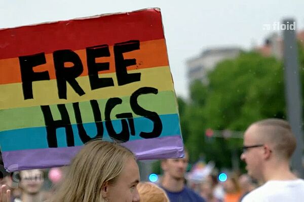 Screenshot einer Sendung von floid: ein Foto vom CSD, Menschen tragen ein Regenbogenplakat mit der Aufschrift Free Hugs