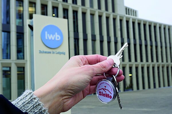 Hand mit einem Schlüssel vor einem Gebäude der LWB