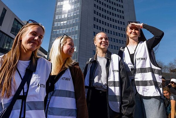 Studentinnen des Seminars "Veranstaltungsmanagement" Vier Studierende der HTWK, die Hochschul-Westen tragen, zum Team der Fakultät gehören und vor der Moritzbastei stehen, , sichten die Lage.