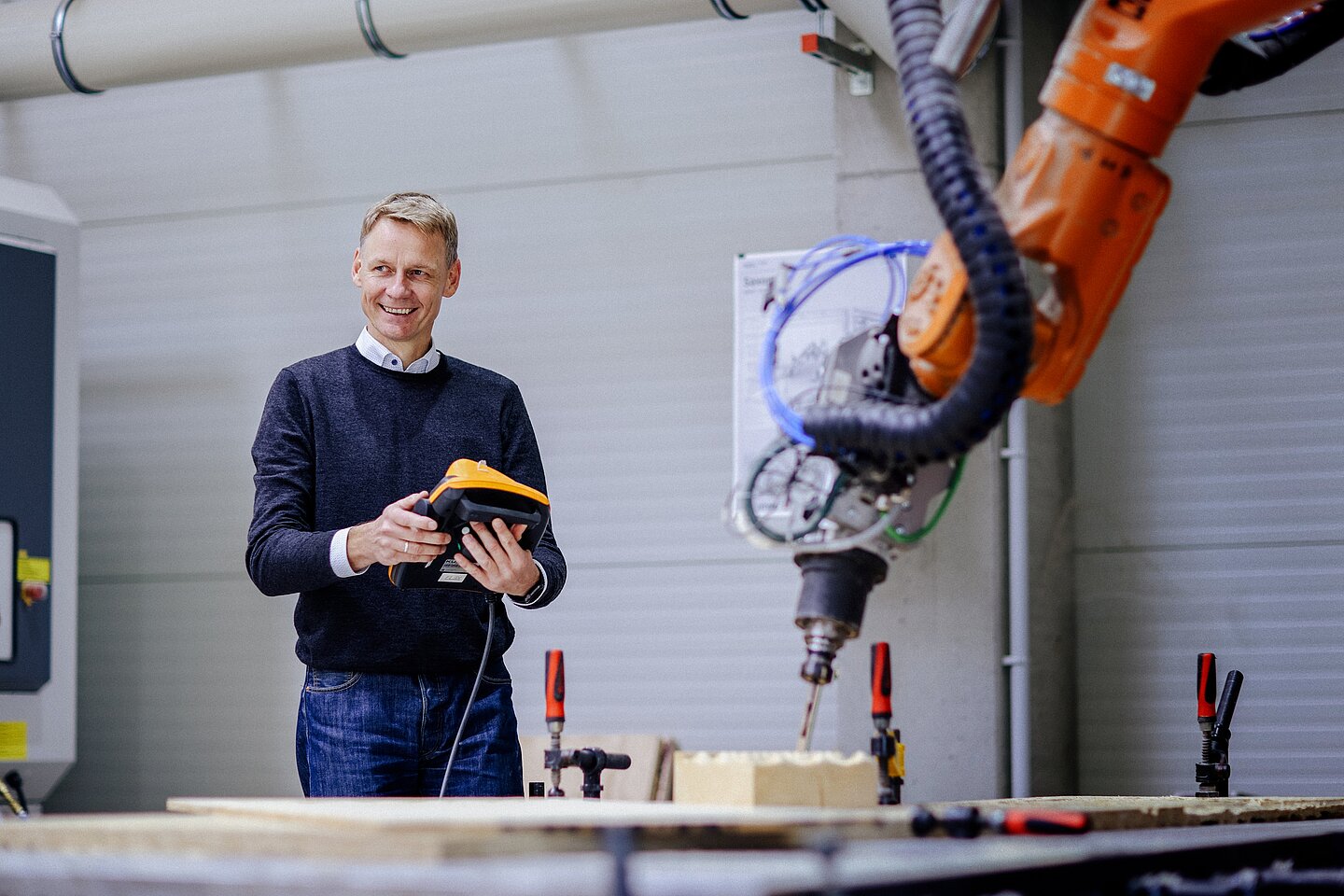 Steuerung einer Maschine Person bedient ein Steuergerät vor einer großen Industrieroboteranlage in einer Werkhalle der HTWK Leipzig.
