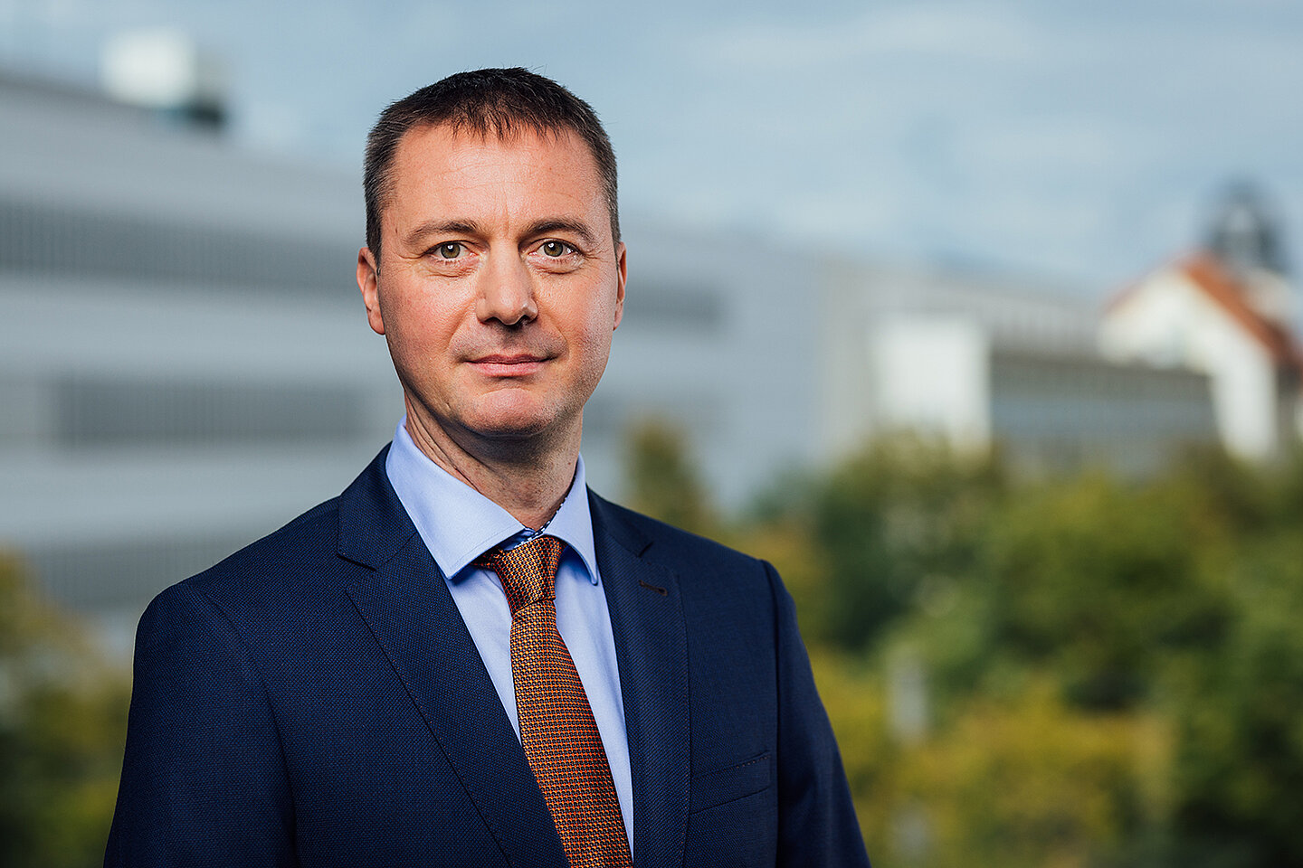 Portrait einer lächelnden Person vor einem Hochschulgebäude 