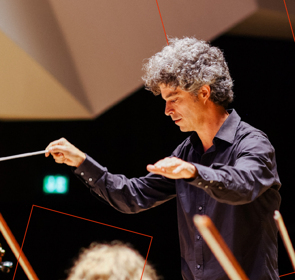 Dirigent mit gehobenen Armen vor seinem musizierenden Orchester.
