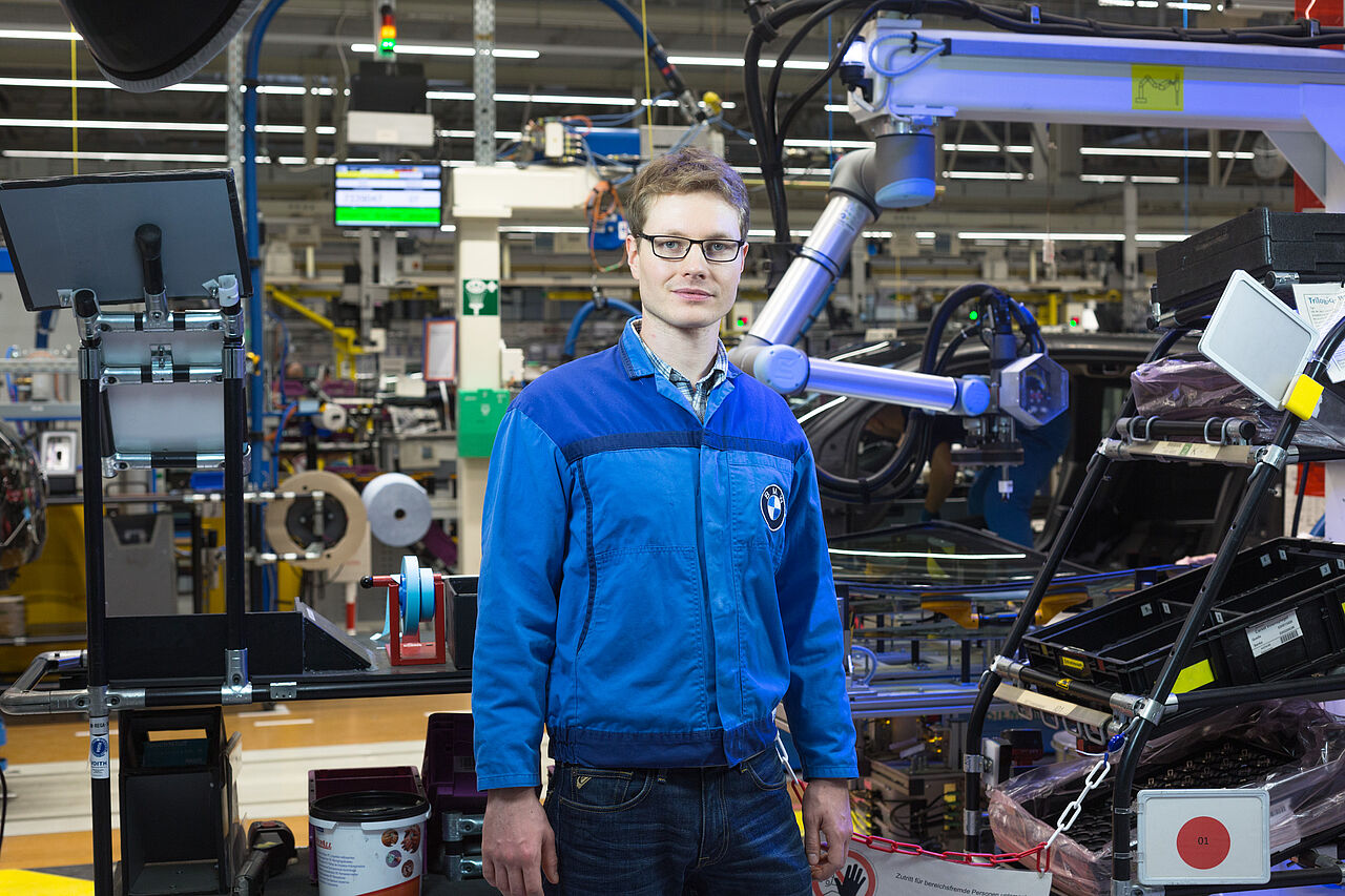 Dr. Robert Brauer in blauer Werkskleidung vor Maschinen im Leipziger BMW-Werk