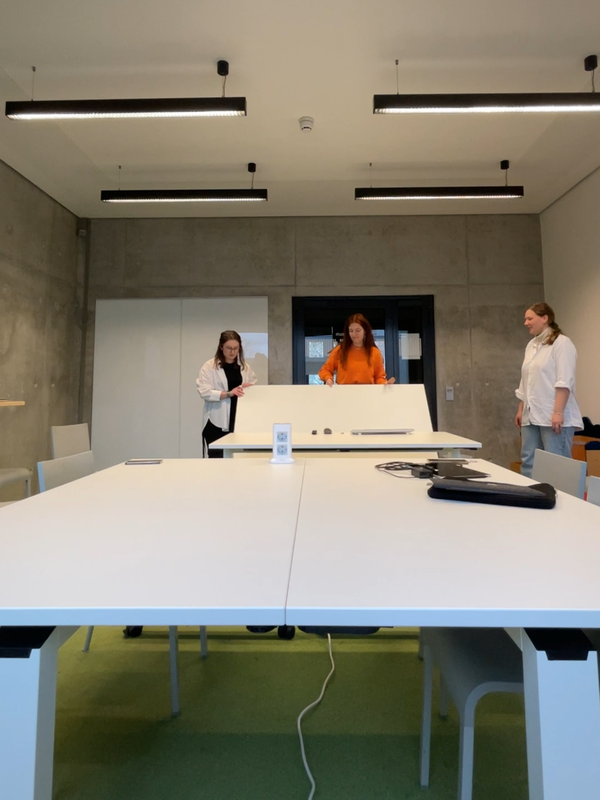 3 Studentinnen räumen im Gruppenarbeitsraum die mobilen Tische um