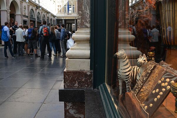 Innenblick in eine edle Passage. In der Mall steht eine Gruppe, in einem Schaufenster ist Schokolade zum Kauf ausgestellt.