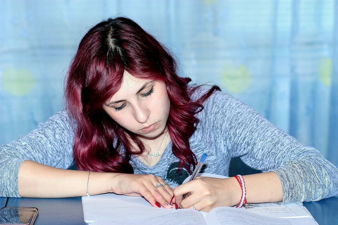 Eine junge Frau mit roten Haaren schreibt in ein Heft