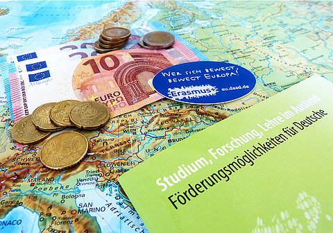 Förderprogramme: Erasmus+ und PROMOS Euros und Heft zu Förderungsmöglichkeiten liegen auf einer Weltkarte