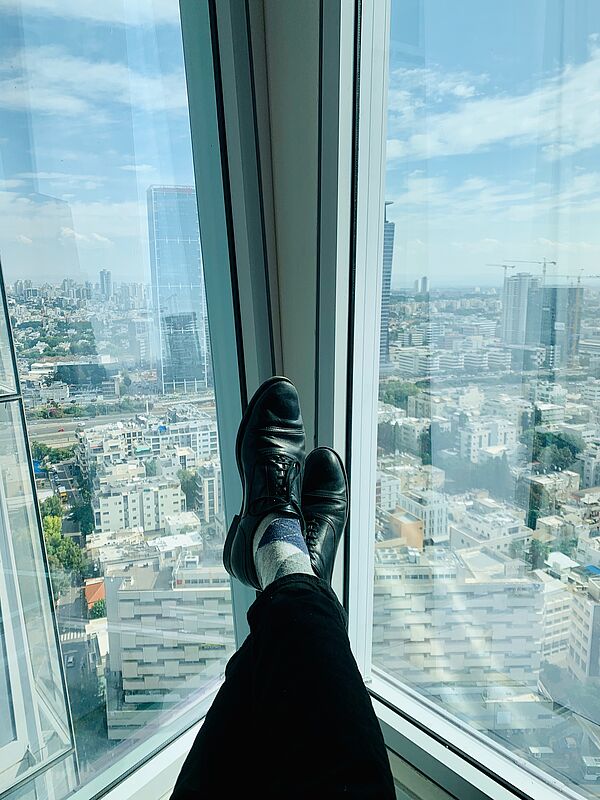 Ein Mann sitzt am Fenster eines Hochhauses und streckt die Beine aus.