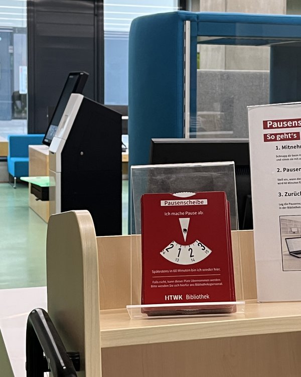 Eine rote Pausenscheibe im Erdgeschoss der Bibliothek, aufgestellt auf einem hölzernen Bücherwagen.