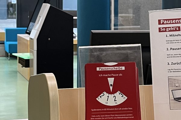 Eine rote Pausenscheibe im Erdgeschoss der Bibliothek, aufgestellt auf einem hölzernen Bücherwagen.