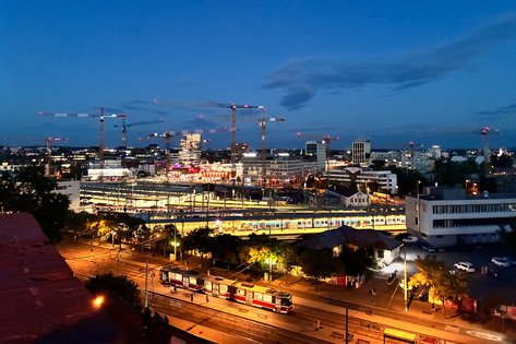 Vogelperspektive, Aufnahme des Bahnhofsviertels nach Sonnenuntergang, leuchtende Straßen und eine Straßenbahn fährt vorbei