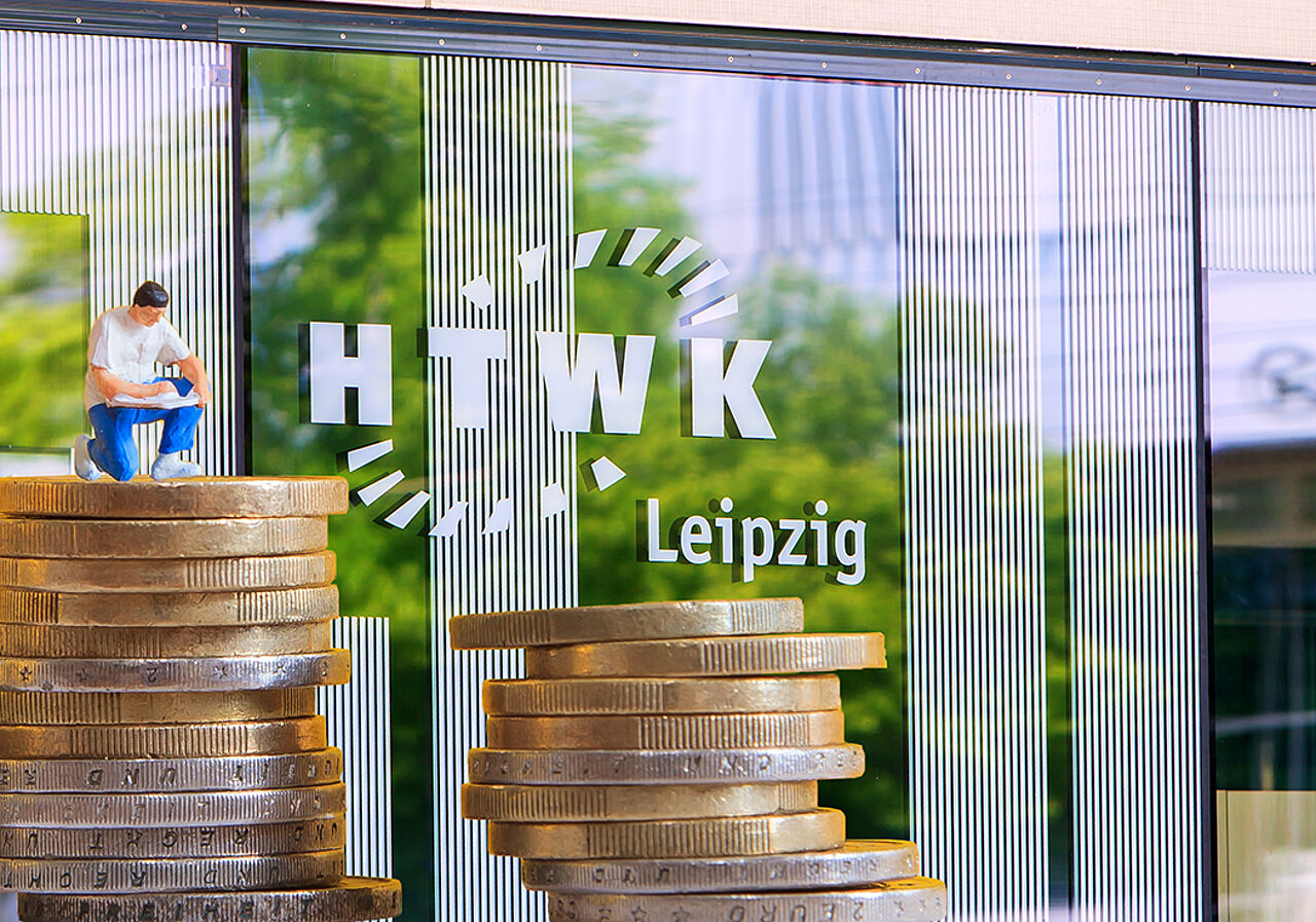 Auf dem Bild sind zwei gestapelte Münzhaufen zu sehen, wobei der linke höher ist und auf ihm ein Miniaturmännchen platziert wurde. Im Hintergrund ist eine Glasfront und das HTWK Leipzig Logo zu sehen.