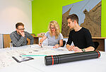 Drei Studierende der Architektur arbeiten an einem Tisch. Hinter ihnen an der Wand steht ein Modell