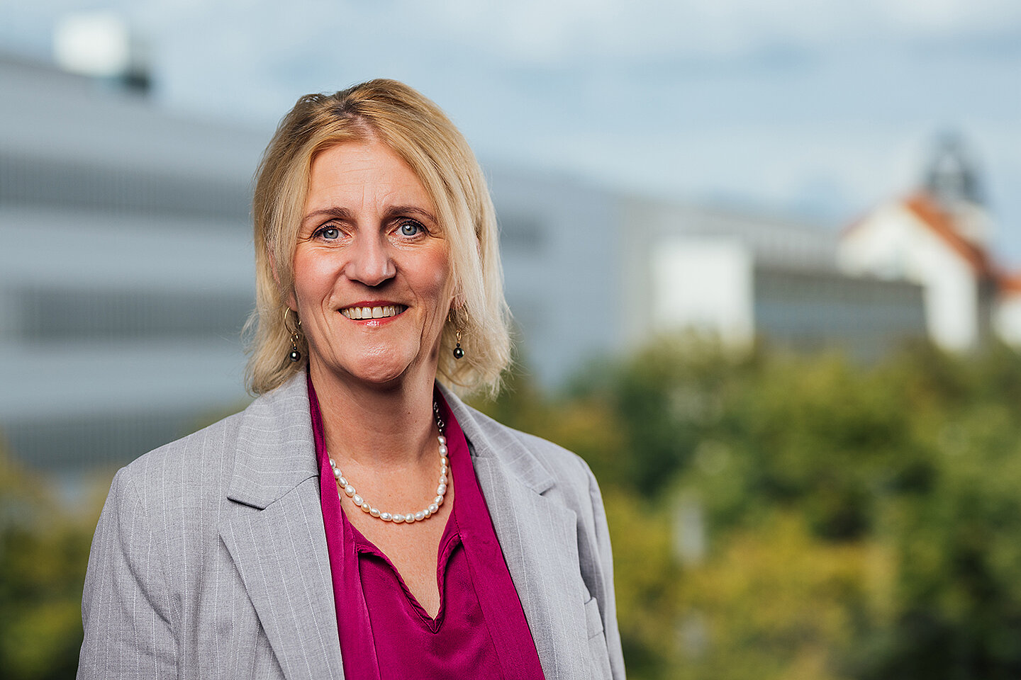Portrait einer lächelnden Person vor einem Hochschulgebäude 
