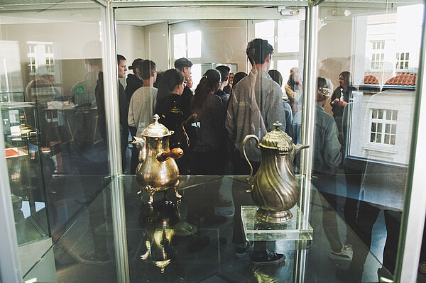 Gruppe von Menschen hinter Vitrine mit alten Kannen