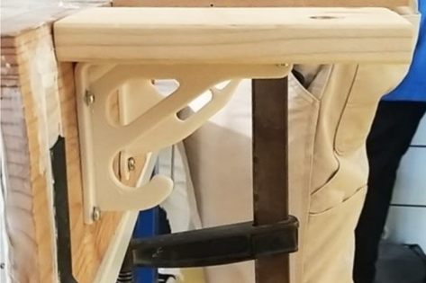 Nahaufnahme eines dunklen Elementes mit schmaler Regalauflage an einem Holzblock befestigt