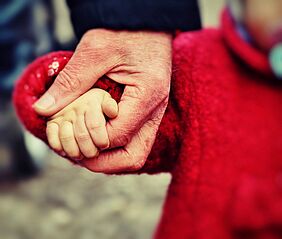 Hand einer älteren Person hält Hand eines kleinen Kindes