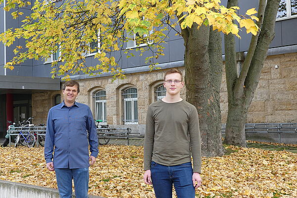 Zwei Männer unter herbstlichem Baum.