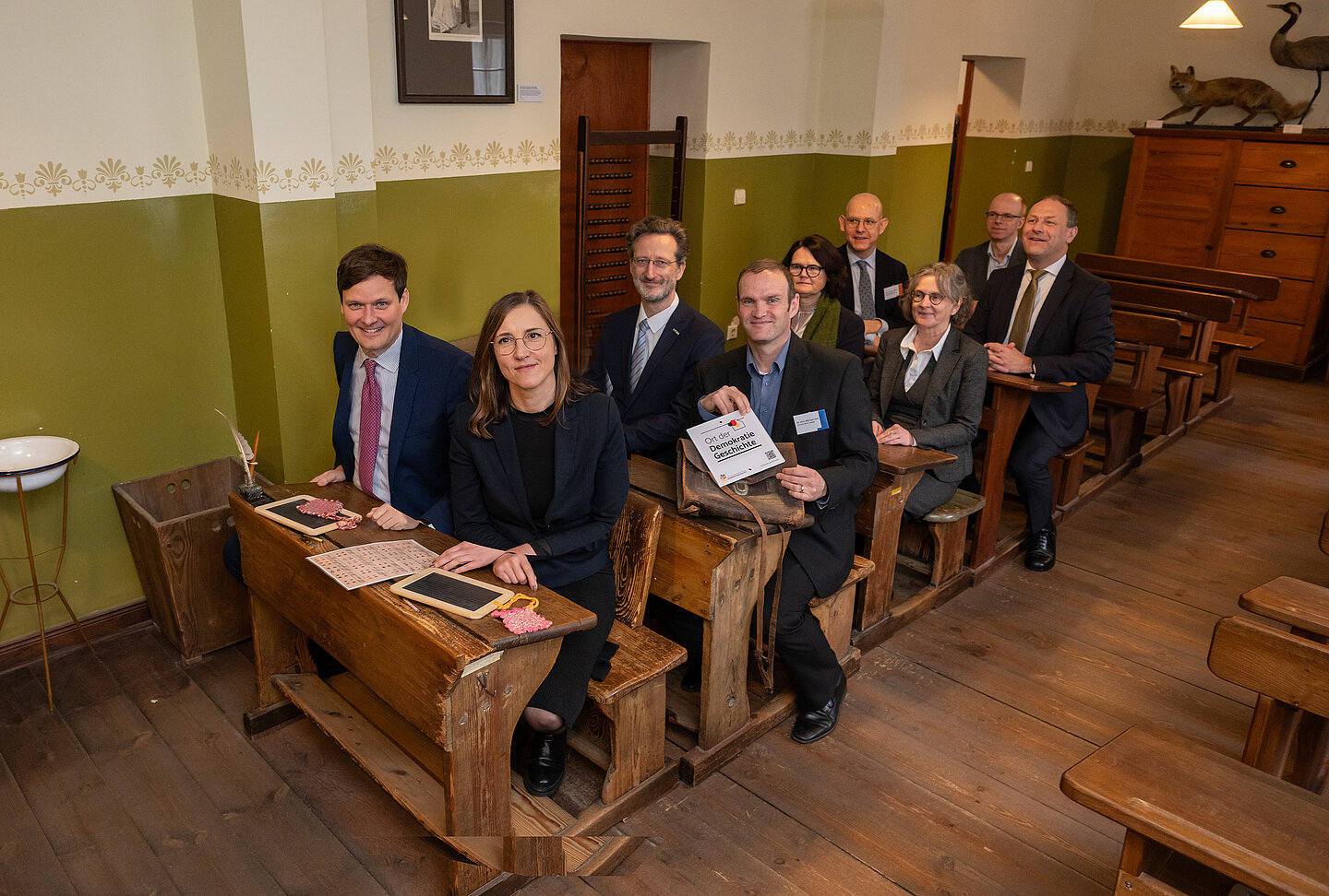 Die Festgesellschaft nimmt Platz im alten Klassenzimmer. (Foto: Eric Kemnitz) Erwachsene sitzen in alten Schulbänken in historischem Klassenzimmer