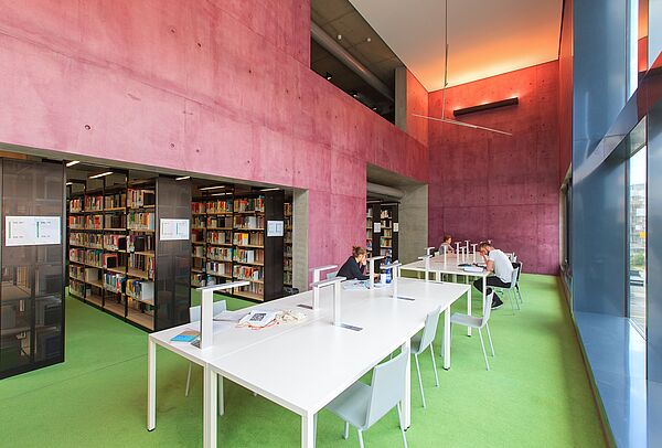 Drei Personen sitzen mit Abstand an Tischen in der Bibliothek.