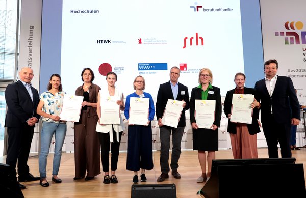 HTWK-Kanzlerin Prof.in Swantje Rother (3. v. re.) mit dem Zertifikat auf der Festveranstaltung. (Foto: Jens Schicke/ berufundfamilie Service GmbH) Gruppe von Menschen mit Urkunden auf einer Bühne
