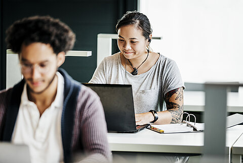 Studierende beim Arbeiten Zwei Studierende sitzen jeweils vor ihrem Laptop an Arbeitstischen.