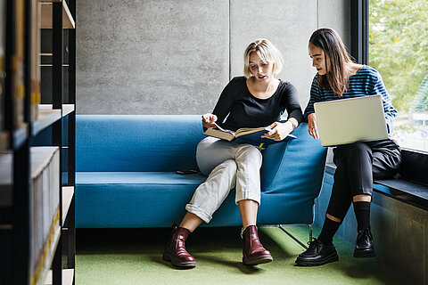 Mentoring unter Studierenden Zwei Studierende gehen gemeinsam Studienmaterial in der Bibliothek durch.