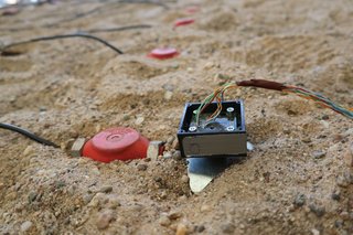 SIMPeL A small sensor with cables lies in the sand; next to it are red measurement points
