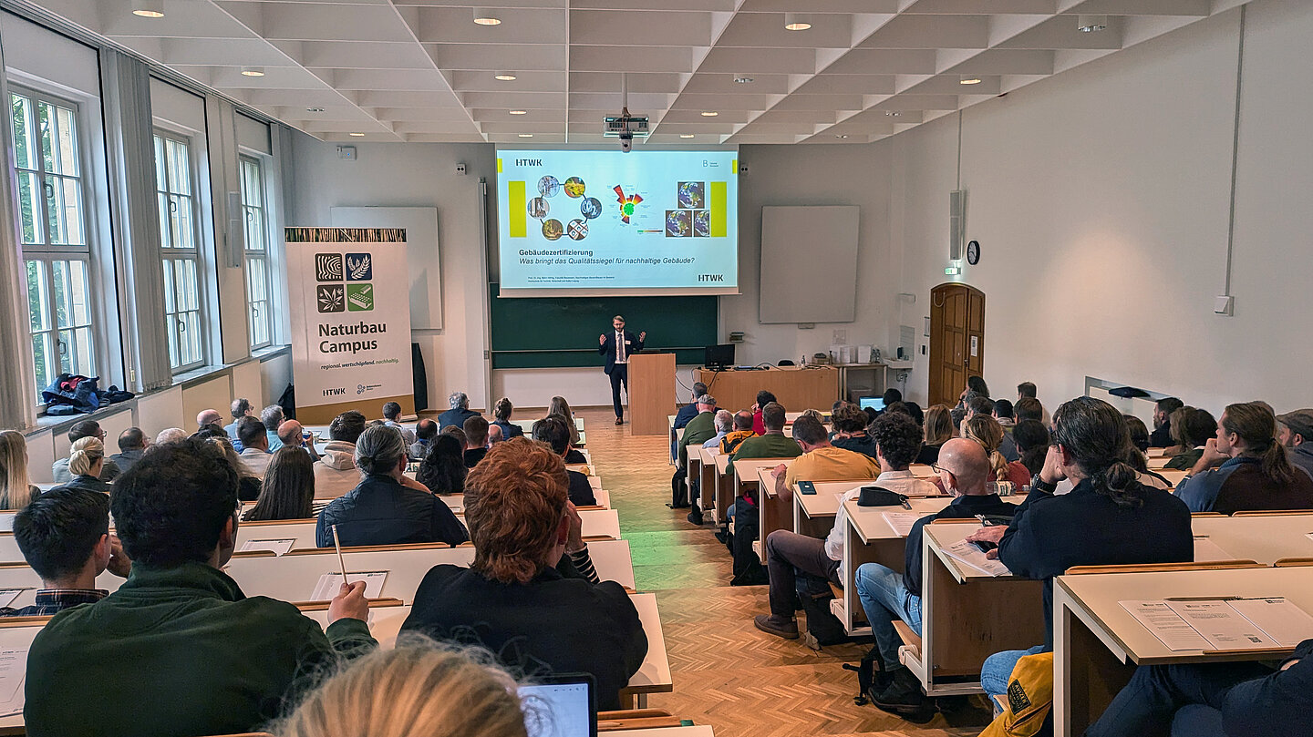Menschen sitzen im Hörsaal und vorne spricht ein Redner.