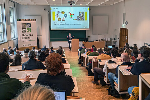Vortrag Nachhaltig Bauen und Sanieren Menschen sitzen im Hörsaal und vorne spricht ein Redner.