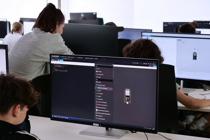 Schülerinnen und Schüler sitzen vor Monitoren, auf dem Bildschirm sieht man Schaltungen von Sensortechnik