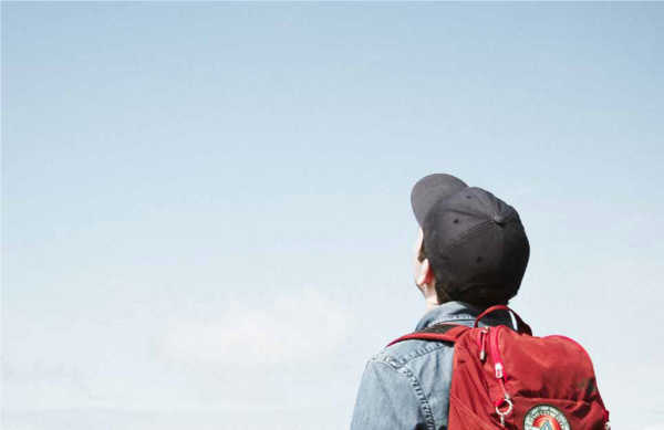 Junge mit Cap und Rucksack schaut in den Himmel