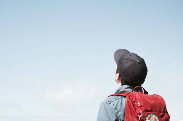 Junge mit Cap und Rucksack schaut in den Himmel