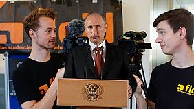 Screenshot der Sendung: zwei floid-Teammitglieder mit Kameras zusammen mit Vladimir Putin auf der Bühne