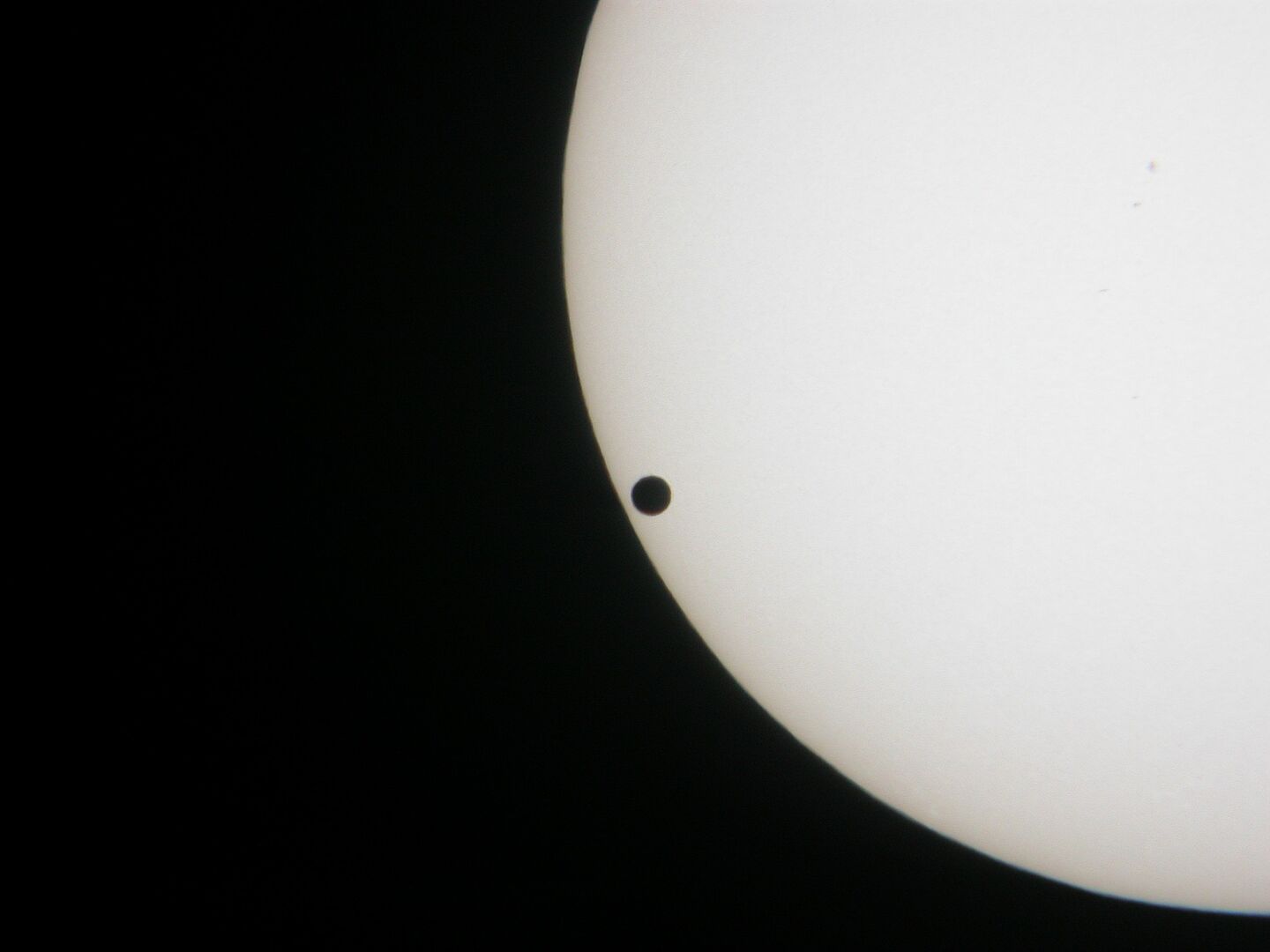 Venustransit 2004 (Foto: Dietmar Telschow) Zu sehen ist das untere linke Viertel der Sonne im Weiß-Licht, vor ihr ist die Venus als schwarzer Punkt zu sehen.