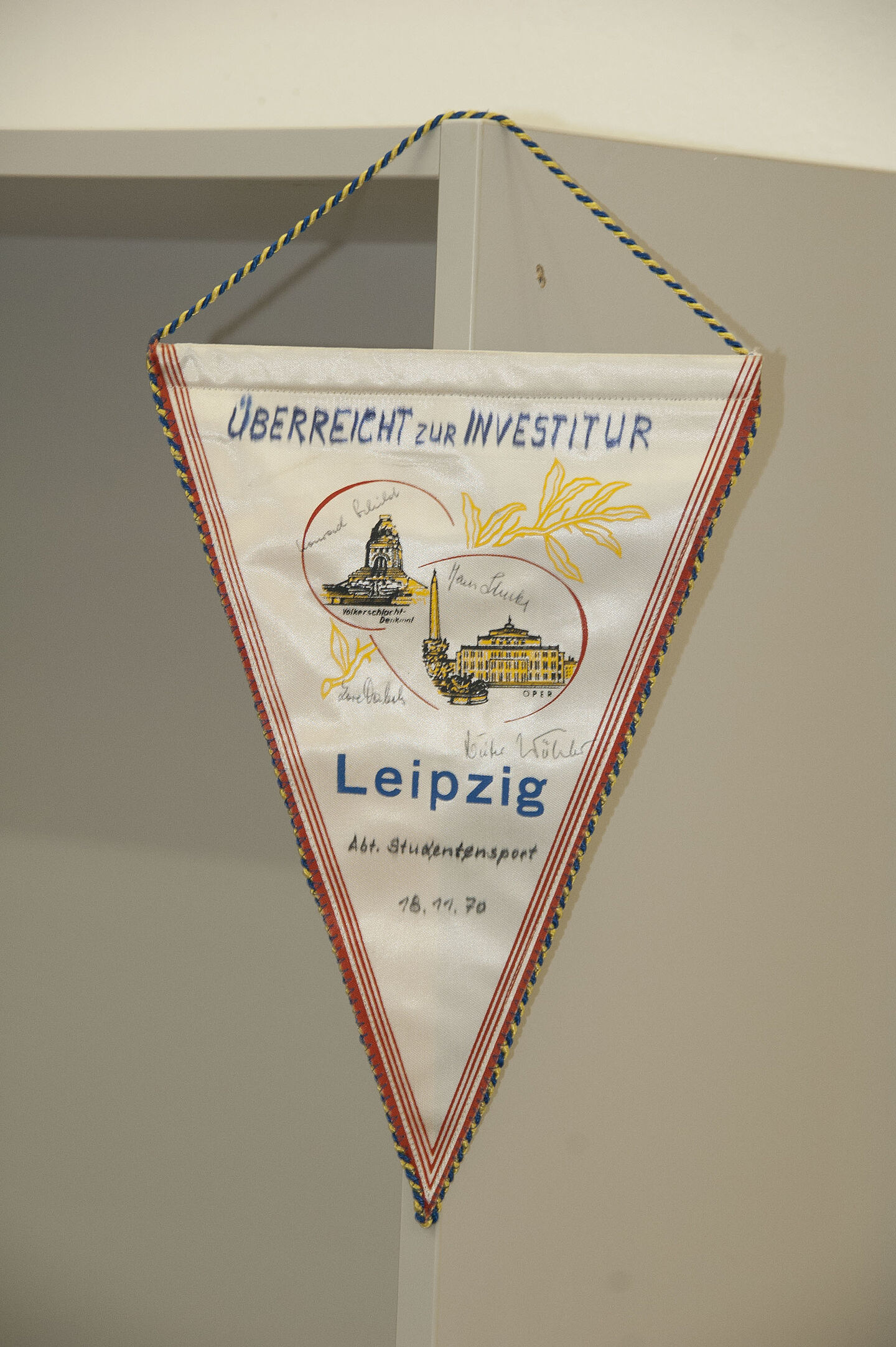 Wimpel aus dem HTWK-Archiv (Foto: HTWK Leipzig) Zu sehen ist ein dreieckiger Wimpel aus weißem Stoff. Darauf steht: "Überreicht zur Investitur. Leipzig Abteilung Studentensport. 18. November 1970".