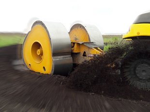 Baumaschine mit gelber Walze verdichtet Boden