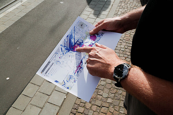 Tilo Sahlbach steht am Friedrich-List-Platz und hält eine ausgedruckte Starkregengefahrenkarte in der Hand.