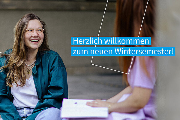 Studentin sitzt freudestrahlend im Trefftz-Bau Eingangsbereich und unterhält sich mit einer Kommilitonin. Auf dem Bild befindet sich der Text "Herzlich willkommen zum neuen Wintersemester!"