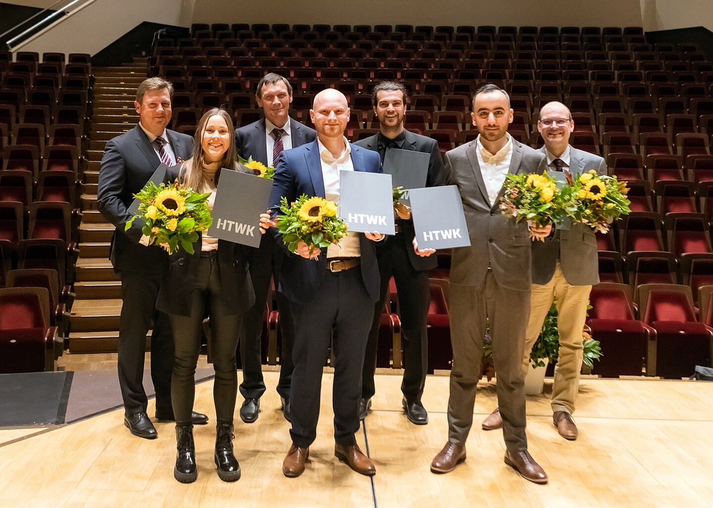 Mehrere Frauen und Männer je mit Blumenstrauß in der Hand stehen auf der Bühne im großen Saal des Gewandhauses