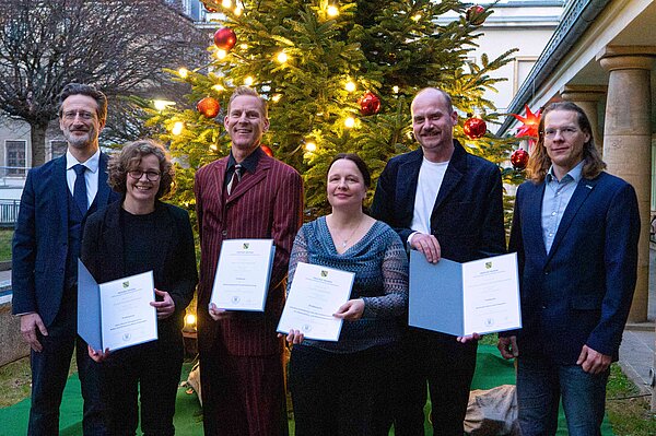 Gruppe von sechs Personen steht vor großem Weihnachtsbaum