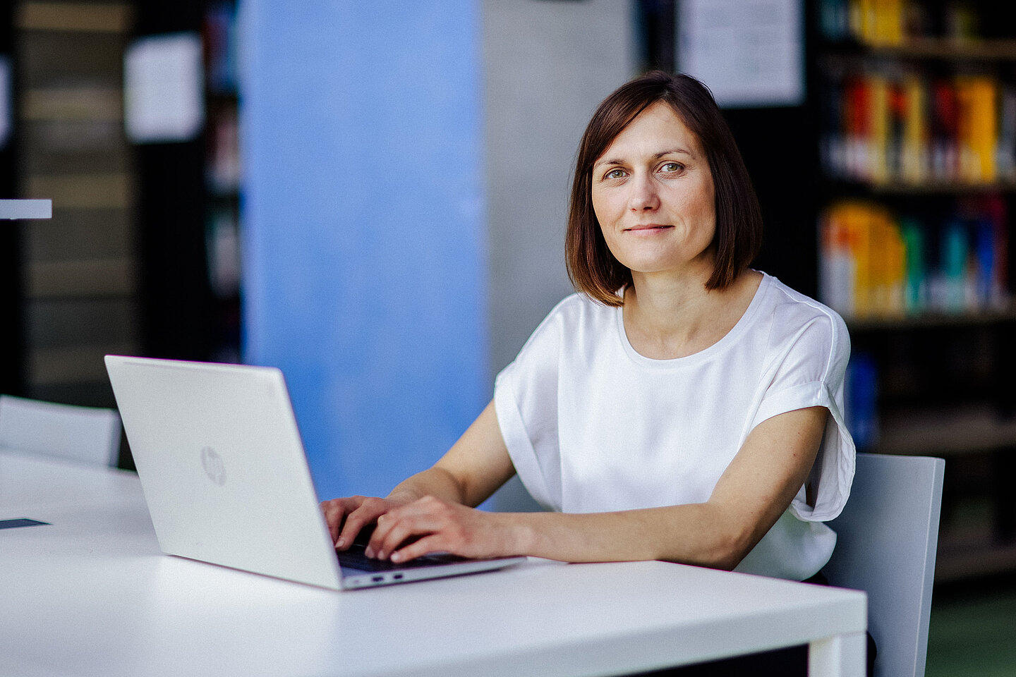 Lächelnde Frau sitzt in der modernen HTWK-Bibliothek an einem Arbeitstisch mit Laptop.