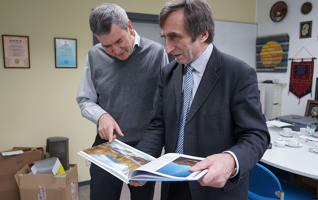 Schauen stehend im Büro auf ein mitgebrachtes Fotoalbum des Altai-Gebirges: Professoren Thomas Kudraß und Klaus Hänßgen
