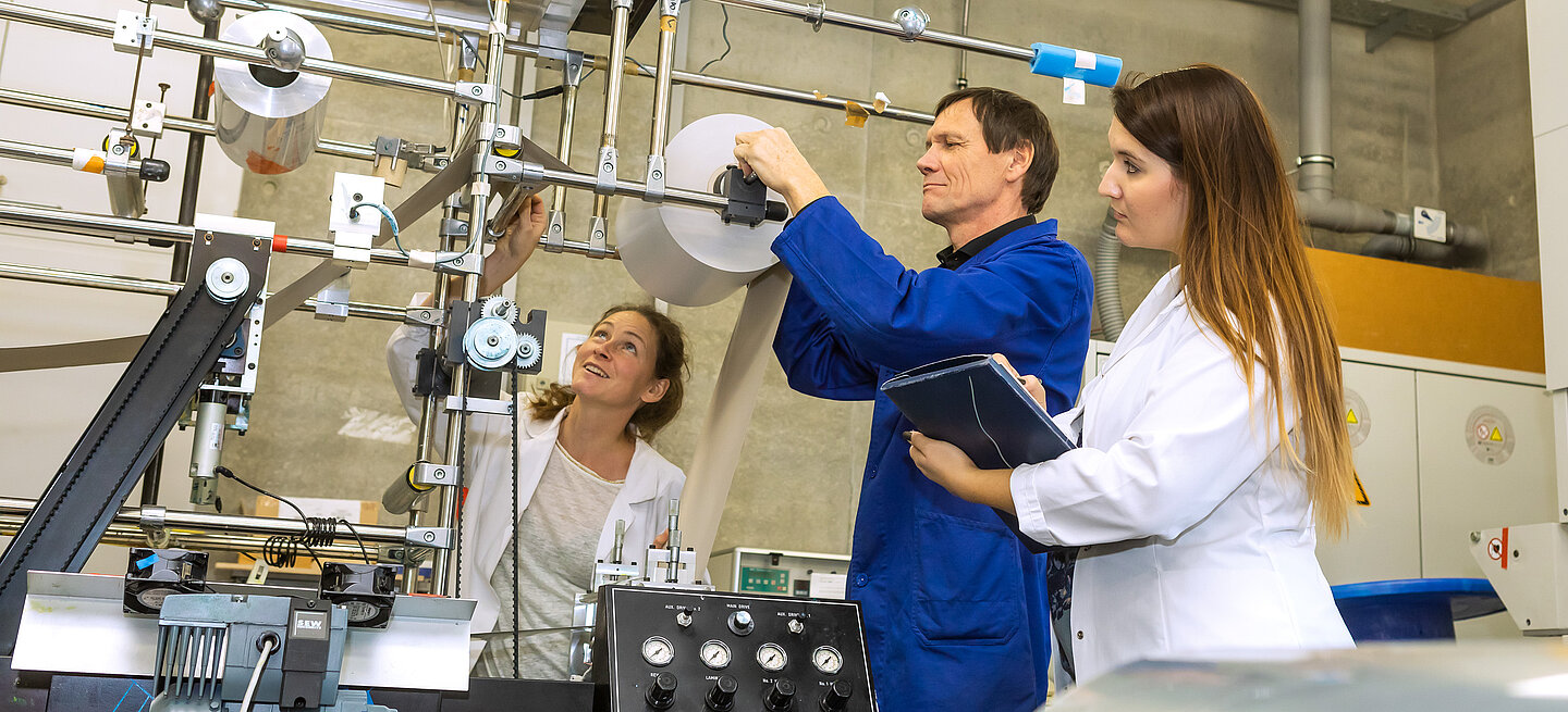 Drei Menschen untersuchen eine Maschine im Labor