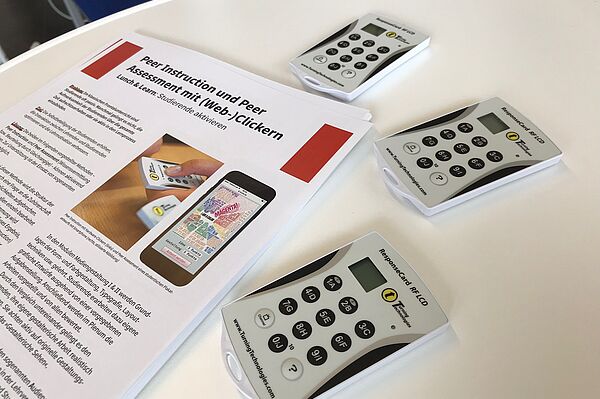 Drei digitale Abstimmungsgeräte (optisch ähnlich Taschenrechnern) und Benutzungshinweise auf einem Tisch.
