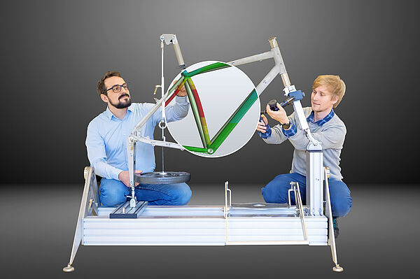 Kjell Bühler (links) und Felix Kaule hocken neben einem Fahrradrahmen und messen