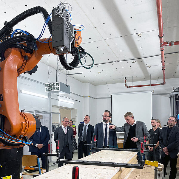 Prof. Alexander Stahr erläutert, wie der Roboter eine Holzrahmenwand zusammenbaut, im Hintergrund stehen mehrere Zuhörer