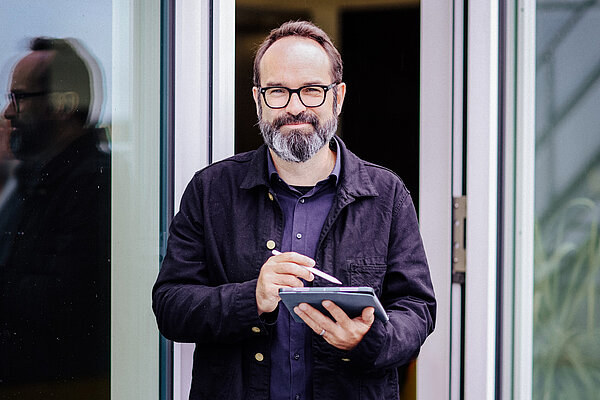 bärtiger Mann mit Laptop lächelt in Kamera