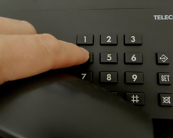 Detailansicht eines schwarzen Telefons mit einer Hand, die den Hörer abnimmt und eine Telefonnummer wählt